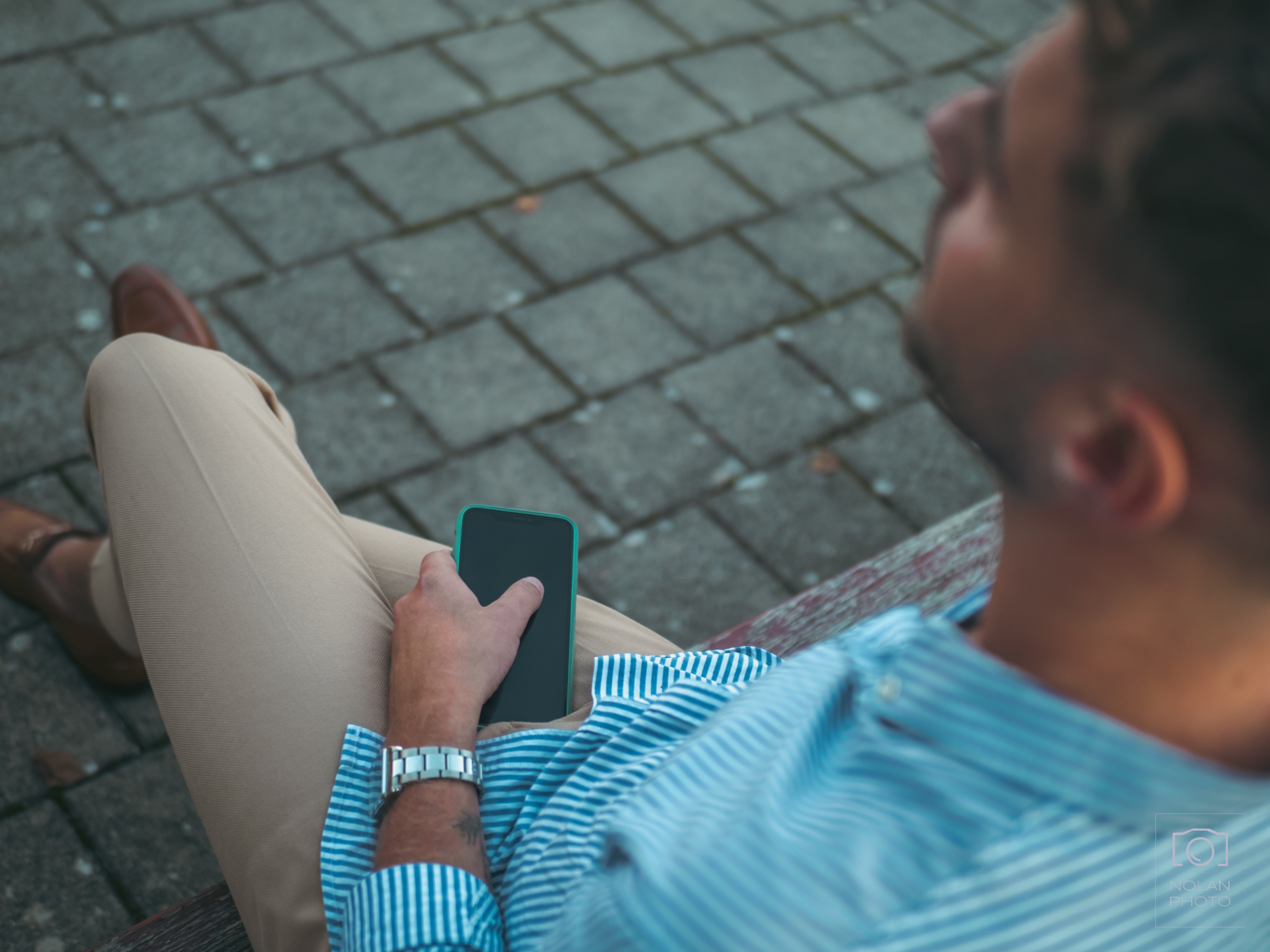 Picture of a man sitting on a bank, with an IPhone in his hand